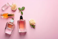 چند شیشه ادکلن مردانه بر روی پارچه صورتی رنگ در کنار برگ و گل رز