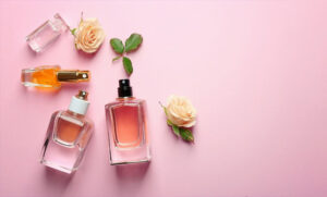 چند شیشه ادکلن مردانه بر روی پارچه صورتی رنگ در کنار برگ و گل رز