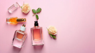 چند شیشه ادکلن مردانه بر روی پارچه صورتی رنگ در کنار برگ و گل رز